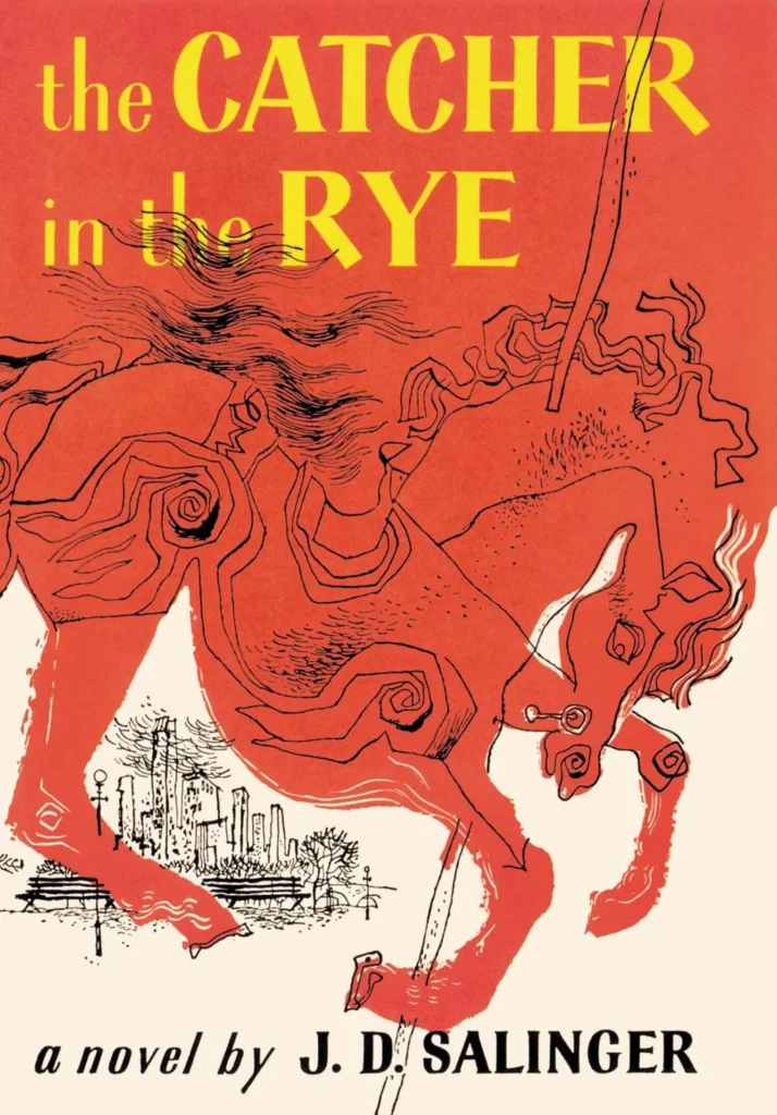 The book cover for The Catcher in the Rye by J.D. Salinger, featuring a red background with the title and author's name in white. The image in the center of the cover is a black and white illustration of a young man wearing a red hunting cap, looking off to the side. This cover image captures the mood of teenage angst and rebellion that is explored in the novel, and suggests the idea of a young person struggling to find their place in the world.